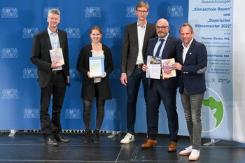 Eine Schülerin und zwei Lehrkräfte posieren mit Herrn Staatsminister Glauber und ihrem Kochbuch und Urkunden.