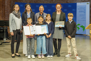 Vier Schülerinnen und Schüler und drei Lehrerinnen der Grundschule an der Haldenbergerstraße posieren mit Herrn Staatsminister Glauber mit Ihren Urkunden.